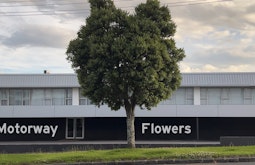 A tree stands in front of a building by a roadside. The words motorway flowers appear on the building